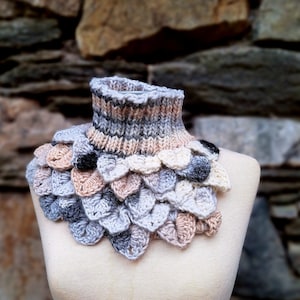 Może przedstawiać: Komin szydełkowy z fakturowanym wzorem w kształcie łusek w odcieniach szarości, beżu i czerni. Komin jest prezentowany na białym manekinie.