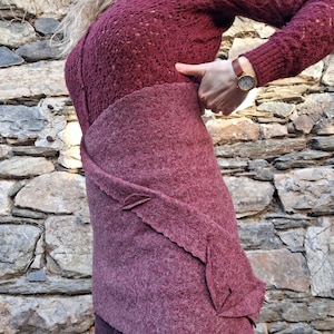 Op de afbeelding: Een bordeauxrode gebreide trui met een losse pasvorm en een delicaat opengewerkt patroon. De trui wordt gedragen over een bordeauxrode rok met een uniek bladvormig ontwerp.