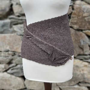 Könnte beinhalten: Ein brauner Strickgürtel mit einem einzigartigen, organischen und strukturierten Design. Der Gürtel wird auf einem weißen Mannequin präsentiert.