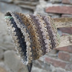 Può includere: Un cappello all'uncinetto in tonalità marrone, grigio e nero. Il cappello è appeso a una recinzione di legno.