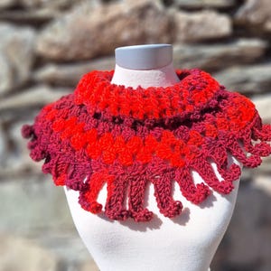 Può includere: Un collo a uncinetto rosso e bordeaux con un bordo a festoni. Il collo è realizzato con un punto a trama e ha una frangia.