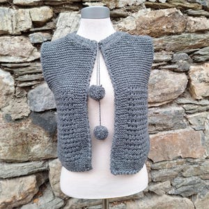 Puede incluir: Un chaleco gris sin mangas de ganchillo con un detalle de pompón en la parte delantera.