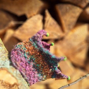 Op de afbeelding: Een kleine, gehaakte kroon in paars, turquoise en bruin. De kroon heeft groene kralen aan de randen.