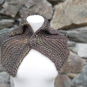 Könnte beinhalten: Ein brauner Strickkragen mit einem strukturierten Muster und einem dezenten goldenen Faden, der durch das ganze Material gewebt ist. Der Kragen ist umgeklappt und auf einer weißen Puppe drapiert.