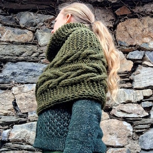 Könnte beinhalten: Olivgrüner Strickschal mit Rollkragen und passendem Pullover. Der Schal ist dick und strukturiert, mit einem markanten Zopfmuster. Der Pullover hat ein Rautenmuster auf der Brust und einen strukturierten Ärmel. Das Outfit ist ein warmer Stil.