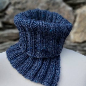 May include: A blue knitted neck warmer with a ribbed texture. The neck warmer is folded over and has a pointed end.