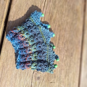 Op de afbeelding: Een blauw, groen en rood gehaakt stuk met groene kralen rond de rand.