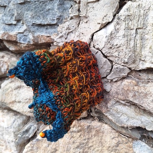 Op de afbeelding: Een kleurrijke gehaakte kroon met oranje kralen, gemaakt van een mix van blauw, oranje, groen en zwart garen.