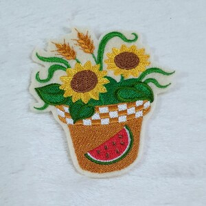Könnte beinhalten: Gestickter Aufnäher mit einem braunen Blumentopf mit einem karierten Muster und einer Scheibe Wassermelone. Der Topf ist mit grünen Blättern und drei gelben Sonnenblumen gefüllt.
