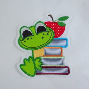 Könnte beinhalten: Grüner Frosch mit einem großen Lächeln, der einen Stapel bunter Bücher mit einem roten Apfel obenauf hält.