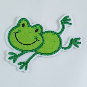 Könnte beinhalten: Grünfilz-Frosch-Applikation mit lächelndem Gesicht und ausgestreckten Gliedmaßen.