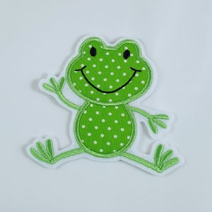 Könnte beinhalten: Grüne Filz-Frosch-Applikation mit weißen Punkten und einem schwarzen lächelnden Mund. Der Frosch hat zwei grüne Filzfüße mit weißen Filz-Zehen.