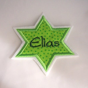 Könnte beinhalten: Grüner Filzstern mit weißem Filzrand und grünen Punkten. Der Name "Elias" ist in Grün auf den Stern gestickt.