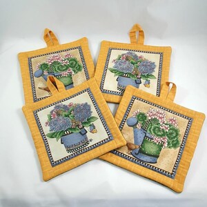 Könnte beinhalten: Set aus vier gelben, gesteppten Topflappen mit Blumenmuster. Jeder Topflappen zeigt ein anderes Blumenarrangement in einer blauen und grünen Gießkanne.