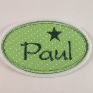 Könnte beinhalten: Grüner, ovaler Stoff-Patch mit weißen Punkten und dem Namen "Paul" in grüner Stickerei. Ein grüner Stern befindet sich über dem Namen.