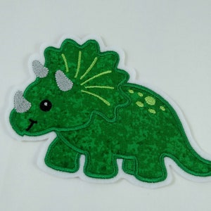Könnte beinhalten: Grün gestickter Bügel-Aufnäher mit einem Cartoon-Triceratops-Dinosaurier mit weißem Umriss.