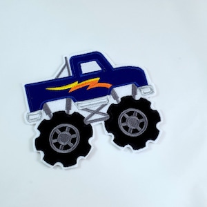 Könnte beinhalten: Blaue Monstertruck-Applikation mit einem gelben Blitz-Design. Der Truck hat schwarze Reifen mit grauen Felgen.