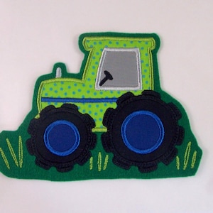 Könnte beinhalten: Grüner und blauer Traktor-Applikator mit schwarzen Rädern und grünem Gras. Der Traktor hat ein graues Fenster und weiße Nähte.