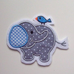 Könnte beinhalten: Ein gestickter Elefant in Grau und Weiß mit einem blauen und orangefarbenen Vogel, der auf seinem Rücken sitzt. Der Elefant hat ein blaues und weißes Gingham-Muster auf seinem Rüssel.