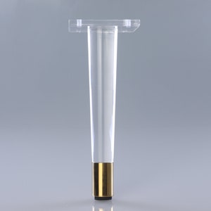 以下が含まれることがあります： 金色の金属製のベースと黒いプラスチック製のフットパッドが付いた透明なアクリル製の家具の脚です。