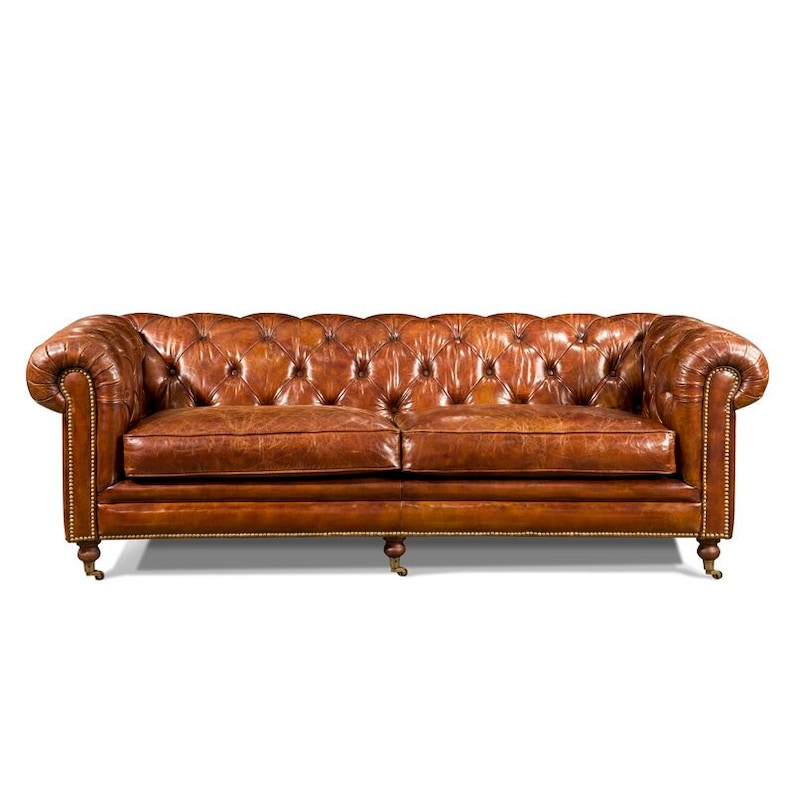 May include: A brown leather sofa with tufted upholstery and brass legs. The sofa has a classic design and is perfect for a traditional living room.
