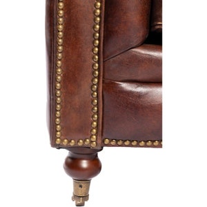 May include: Close-up of a brown leather armchair with brass nailhead trim and wooden legs. The armchair has a tufted back and seat.