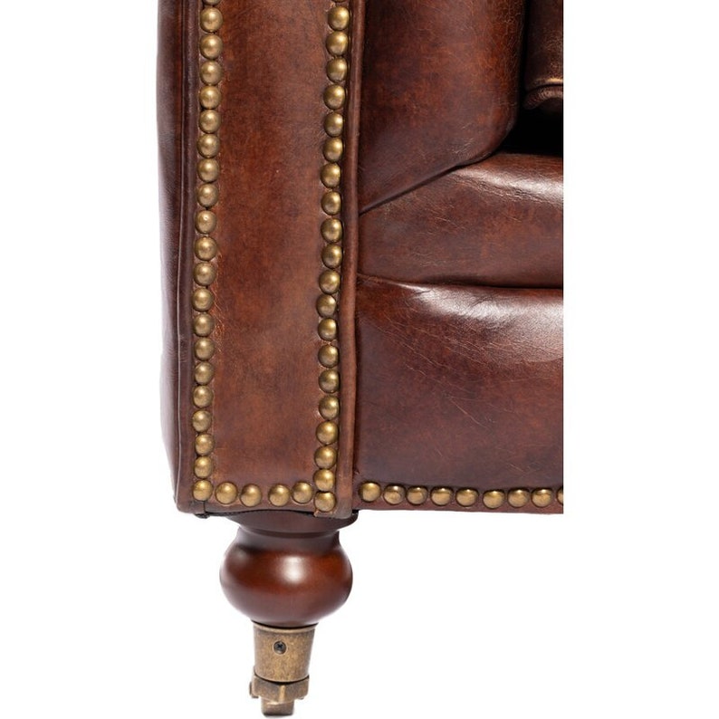 May include: Close-up of a brown leather armchair with brass nailhead trim and wooden legs. The armchair has a tufted back and seat.