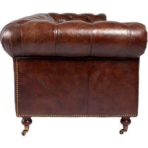 May include: A brown leather sofa with tufted upholstery and brass nailhead trim. The sofa has a rolled back and arms and sits on wooden legs with casters.