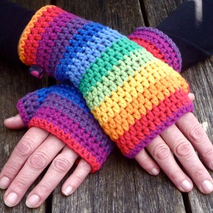 Könnte beinhalten: Ein Paar regenbogenfarbene Fingerlose-Handschuhe aus Häkelarbeit. Die Handschuhe sind aus verschiedenen Farben gefertigt, darunter Rot, Orange, Gelb, Grün, Blau, Indigo und Violett.