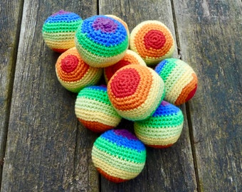 Könnte beinhalten: Eine Gruppe von acht gehäkelten Regenbogenbällen, jeder mit einem anderen Farbmuster. Die Bälle sind aus verschiedenen Farben hergestellt, darunter Rot, Orange, Gelb, Grün, Blau und Lila. Die Bälle sind auf einer Holzoberfläche zu einem Stapel angeordnet.