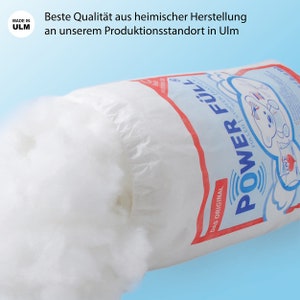 Peut inclure: Un sac blanc rempli de rembourrage blanc et moelleux. Le sac porte une inscription rouge et bleue qui dit "POWER F&Uuml;LL" et "DAS ORIGINAL". Un petit cercle rouge avec le texte "MADE IN ULM" se trouve dans le coin sup&eacute;rieur gauche.