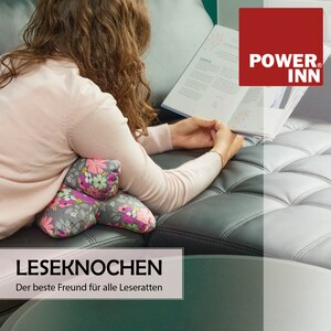 May include: A woman relaxes on a couch with a book and a floral patterned reading pillow. The pillow is shaped like a bent arm and is designed to support the reader's neck and back. The text on the pillow reads "LESEKNOCHEN Der beste Freund f&uuml;r alle Leseratten".