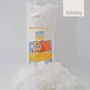 Peut inclure: Un sac transparent rempli de fibres de polyester blanches, étiqueté "soft füll" avec un ours en peluche et une illustration d'oreiller orange. Le sac est marqué "5000g" et une pile de fibres est devant.