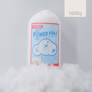 Op de afbeelding: Een witte zak met 500 g Power Füll vulling voor het vullen en stoppen van speelgoed. De zak heeft een blauw en rood etiket met een teddybeer en een schaar. Op het etiket staat "Das Original Power Füll Füllen, Stopfen, Basteln".