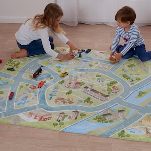 Könnte beinhalten: Eine rechteckige Spielmatte mit einem Stadtplan-Design in Grün, Blau und Beige. Die Matte zeigt Straßen, Gebäude und Wasserflächen. Kinder spielen mit Spielzeugautos und einem Holzeisenbahn-Set auf der Matte.