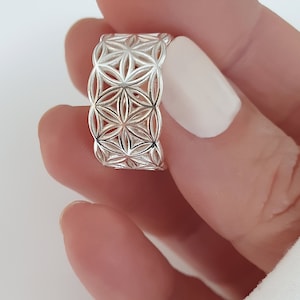 Könnte beinhalten: Ein silberner Ring mit einem geometrischen Lebensblume-Design. Der Ring ist breit und hat ein detailliertes Muster.