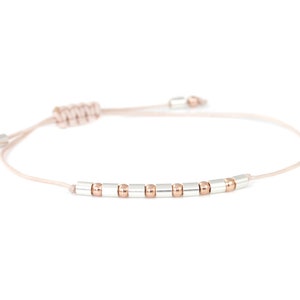 Könnte beinhalten: Ein zartes Armband mit einem rosafarbenen Band und abwechselnd silbernen und roségoldenen Perlen.
