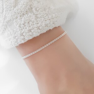 Könnte beinhalten: Ein silbernes Kettenarmband am Handgelenk einer Person. Das Armband besteht aus einer zarten, miteinander verwobenen Kette.