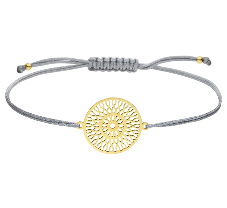 Puede incluir: Un brazalete ajustable de cuerda gris con un colgante circular dorado con un delicado dise&ntilde;o de corte intrincado.