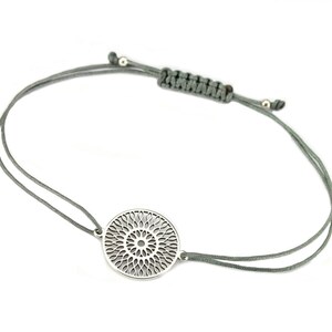 Puede incluir: Un brazalete de plata con un delicado dise&ntilde;o circular de mandala. El brazalete est&aacute; hecho con un cord&oacute;n gris y un cierre ajustable.