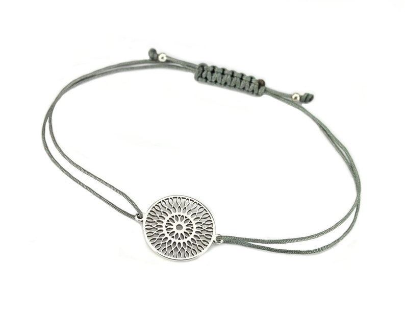 Puede incluir: Un brazalete de plata con un delicado dise&ntilde;o circular de mandala. El brazalete est&aacute; hecho con un cord&oacute;n gris y un cierre ajustable.