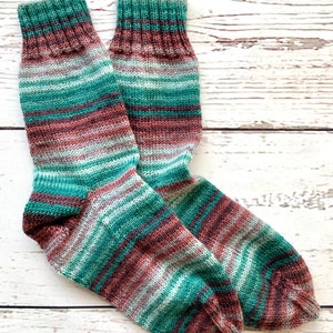 Könnte beinhalten: Ein Paar gestreifte Socken in Grün-, Braun- und Weißtönen. Die Socken sind gestrickt und haben eine strukturierte Oberfläche.
