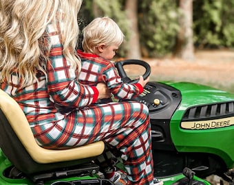 Könnte beinhalten: Eine Frau und ein Kind in passenden rot-weiß-grünen karierten Pyjamas sitzen auf einem grünen John Deere Rasenmäher.