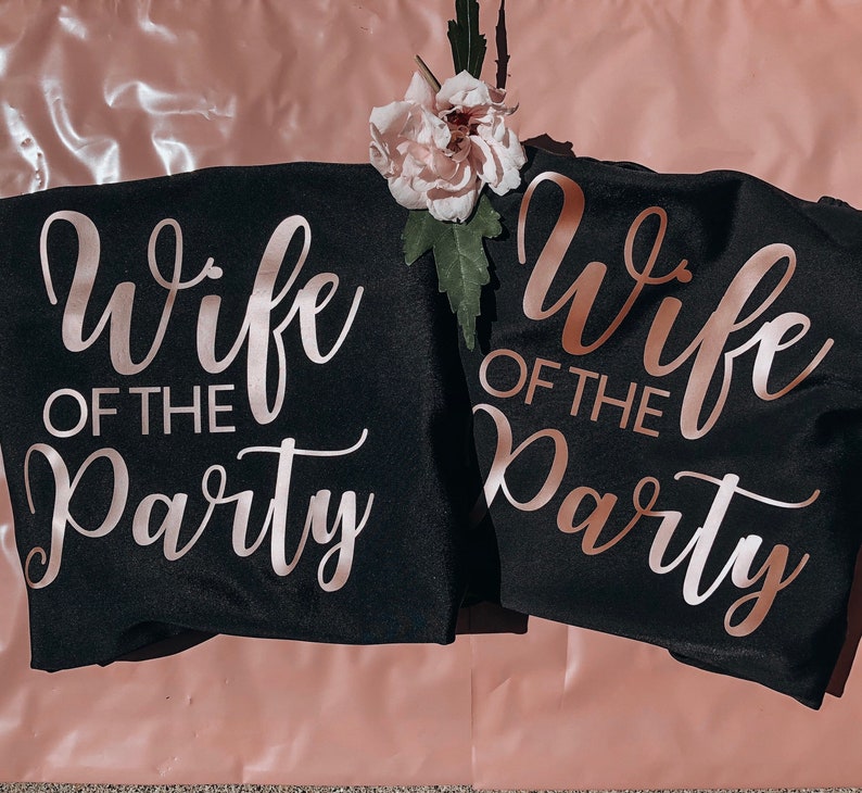 Op de afbeelding: Twee zwarte T-shirts met de tekst "Wife of the Party" in ros&eacute;gouden letters.