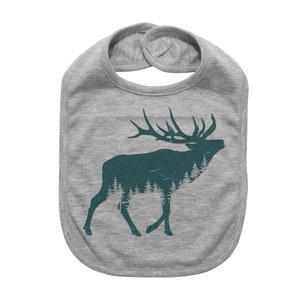 May include: A gray baby bib with a teal elk silhouette design. The elk is filled with a forest scene. The bib has a rounded shape and a snap closure at the neck.