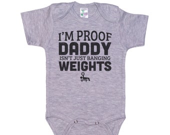 May include: Gray short-sleeved baby bodysuit with black text that reads "I'm Proof Daddy Isn't Just Banging Weights" with a small graphic of a person lifting weights.