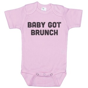 May include: Pink baby onesie with short sleeves and the text "BABY GOT BRUNCH" printed in black.