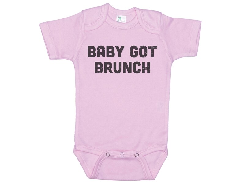 May include: Pink baby onesie with short sleeves and the text "BABY GOT BRUNCH" printed in black.