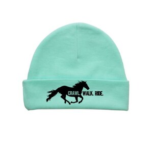 May include: A turquoise beanie with a black silhouette of a horse running and the text "CRAWL. WALK. RIDE."