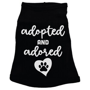 May include: Black dog shirt with white text that says "adopted and adored" with a white paw print inside a heart.